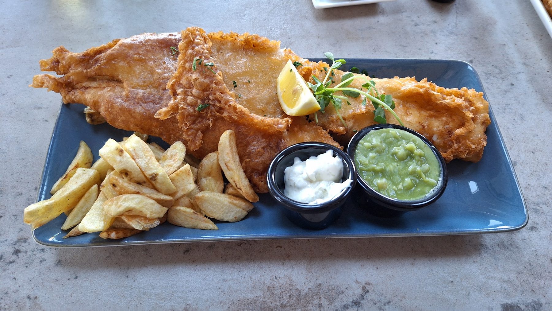 Battered fish and chips with mushy peas and tartare sauce on a blue plate